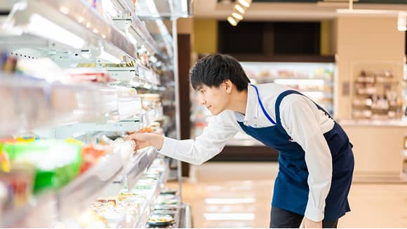 コンビニ店舗で冷蔵ケースの商品を整えるスタッフ